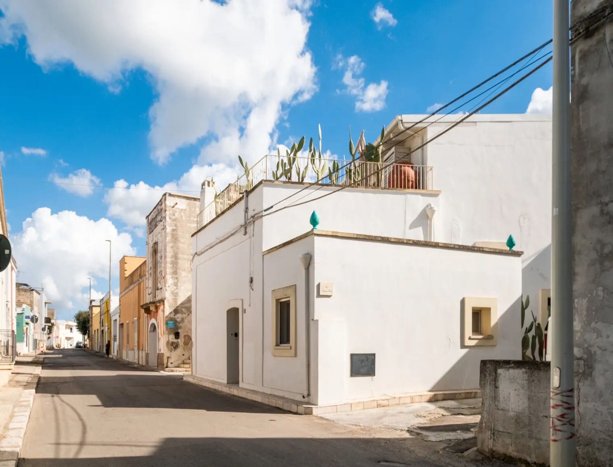 Una calle con edificios, cielo despejado y algunas plantas en los tejados.