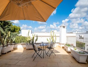 A terrace with a table and chairs, potted plants, and a white building in the background. - Petra Domus Spa & Private Lodge (Veglie)