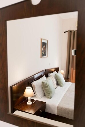Une chambre d’hôtel avec une tête de lit en bois, un lit avec une literie blanche et des oreillers verts, une lampe de chevet, un tableau encadré au mur et une fenêtre avec des rideaux.