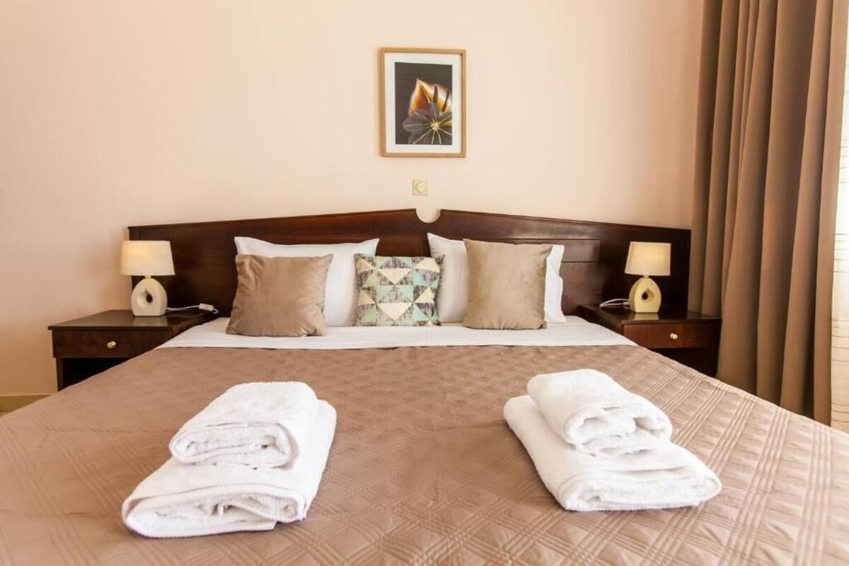 A hotel room with a large bed, two bedside tables with lamps, a framed picture on the wall, and a window with curtains.