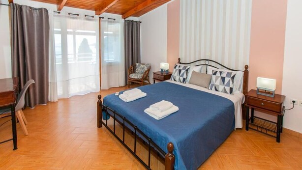 A bedroom with a wooden bed, two bedside tables, a chair, and a desk. - Hotel Thetis (Tolo)