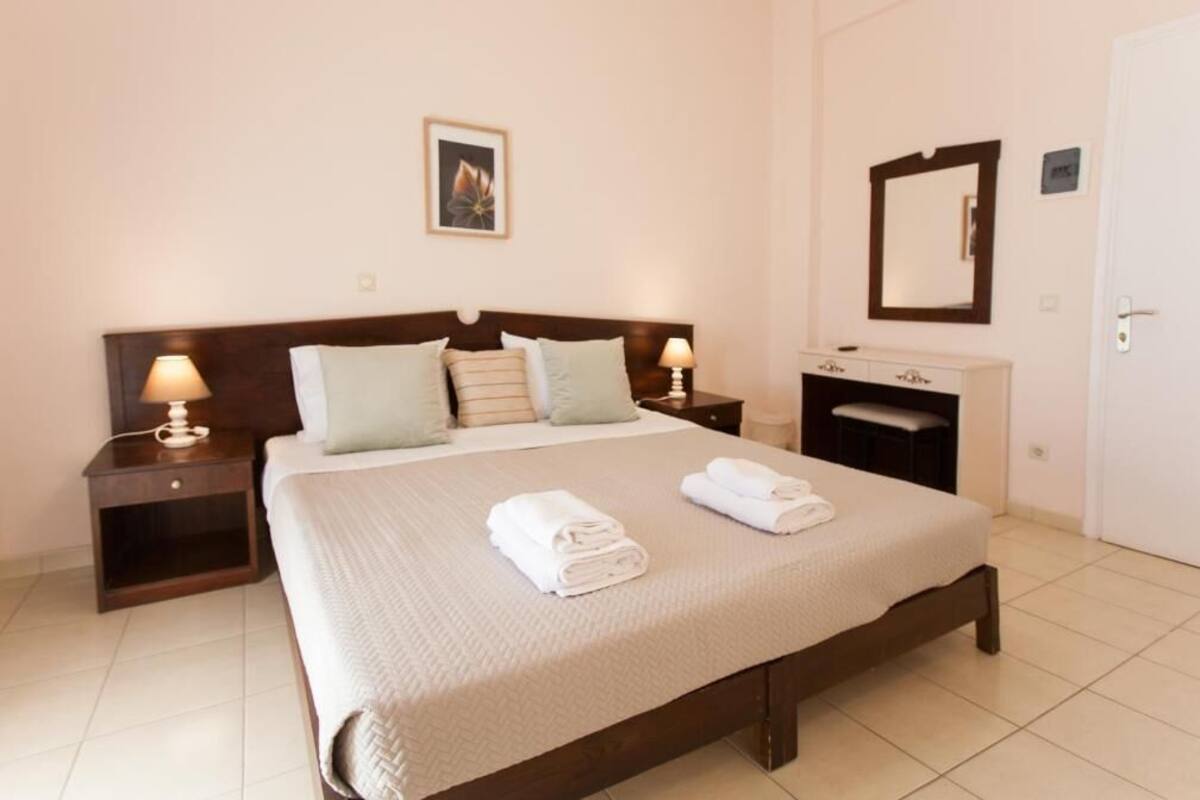 A neatly made bed with pillows, a bedside table with a lamp, a mirror, and a small cabinet.