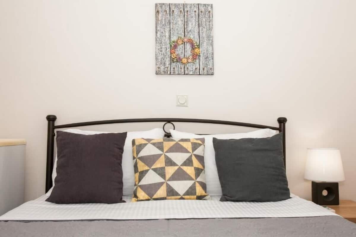 A bed with a headboard, three pillows, a wall-mounted decoration, and a bedside lamp.