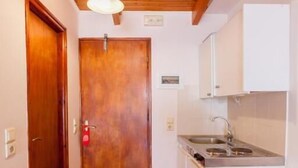 A narrow hallway with a wooden door, a small kitchen area with a sink and cabinets, and a wooden ceiling. - Hotel Thetis (Tolo)