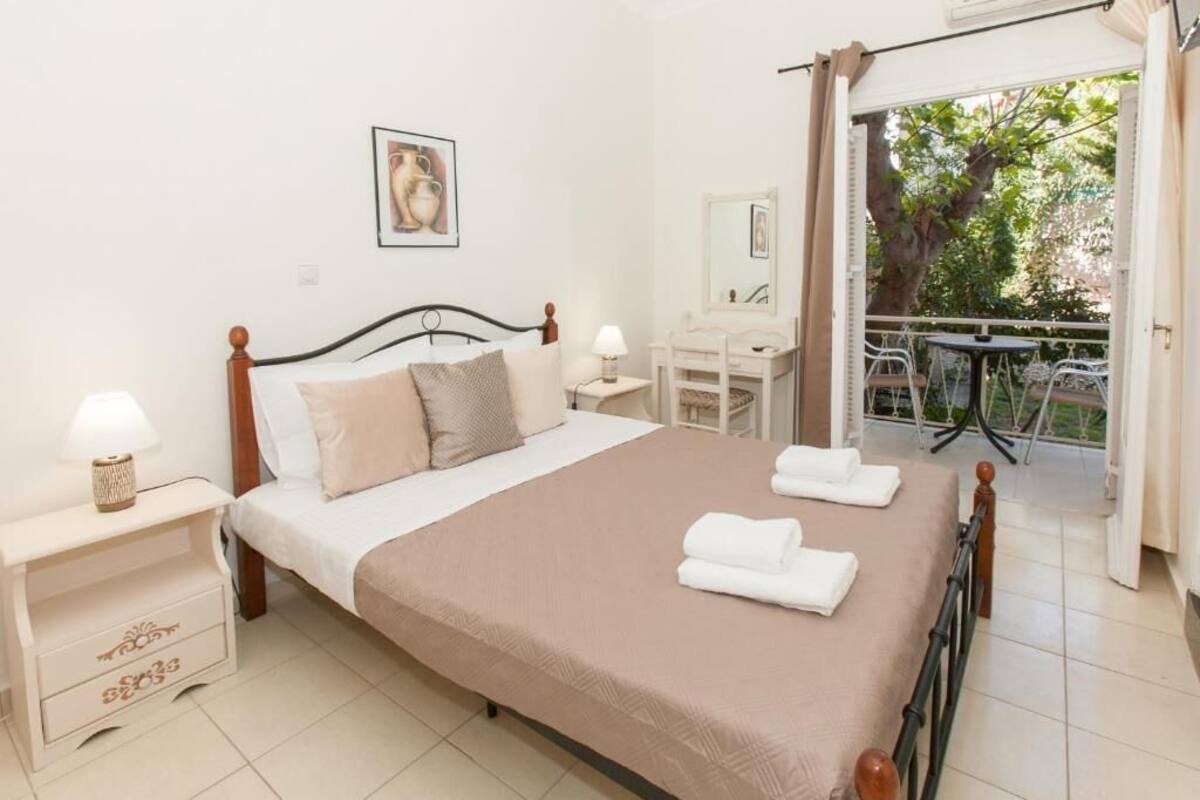 A bedroom with a bed, bedside tables, a mirror, and a balcony with outdoor furniture.
