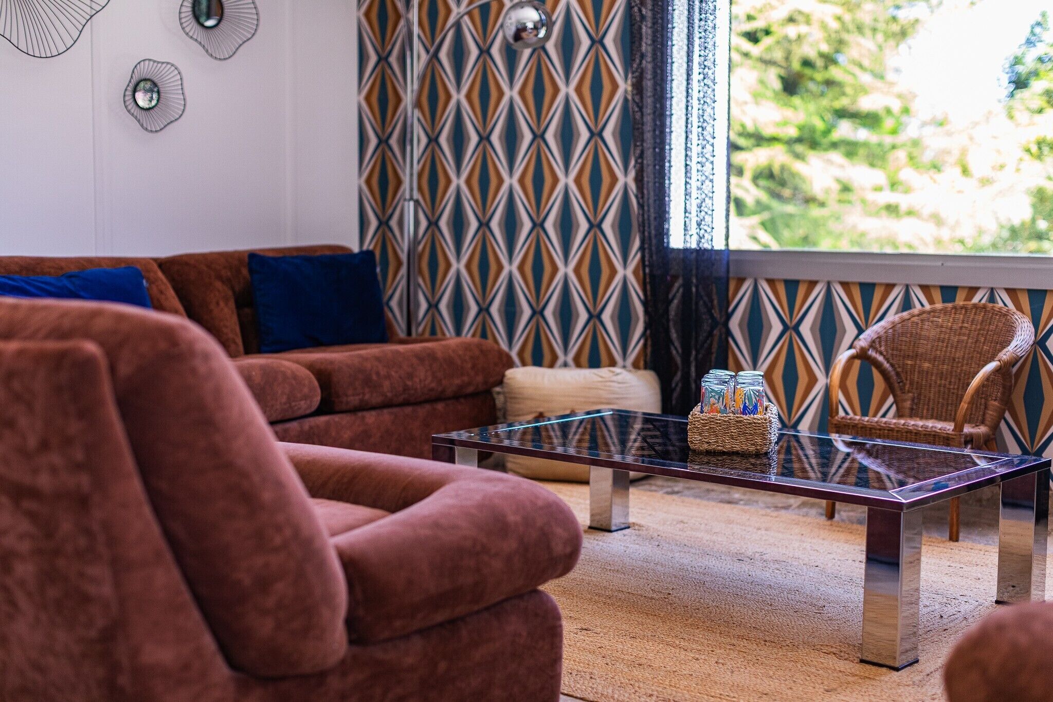 A living room with a brown sofa, a glass coffee table, and a wicker chair.