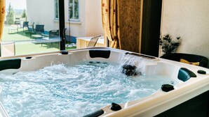 Ein Whirlpool mit Wasserstrahlen, eine Glastür zu einem Außenbereich und Blick auf ein Gebäude und Grünflächen.