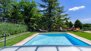 Ein rechteckiger Swimmingpool mit glasklar blauem Wasser, umgeben von einer gepflegten Rasenfläche und verschiedenen Bäumen.