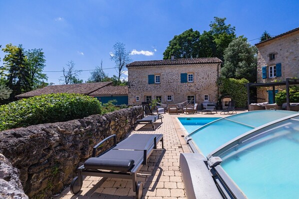 Un bâtiment en pierre doté d’une piscine, de chaises longues et d’un mur en pierre.