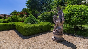 Een standbeeld in een tuin met gesnoeide hagen en een heldere lucht.