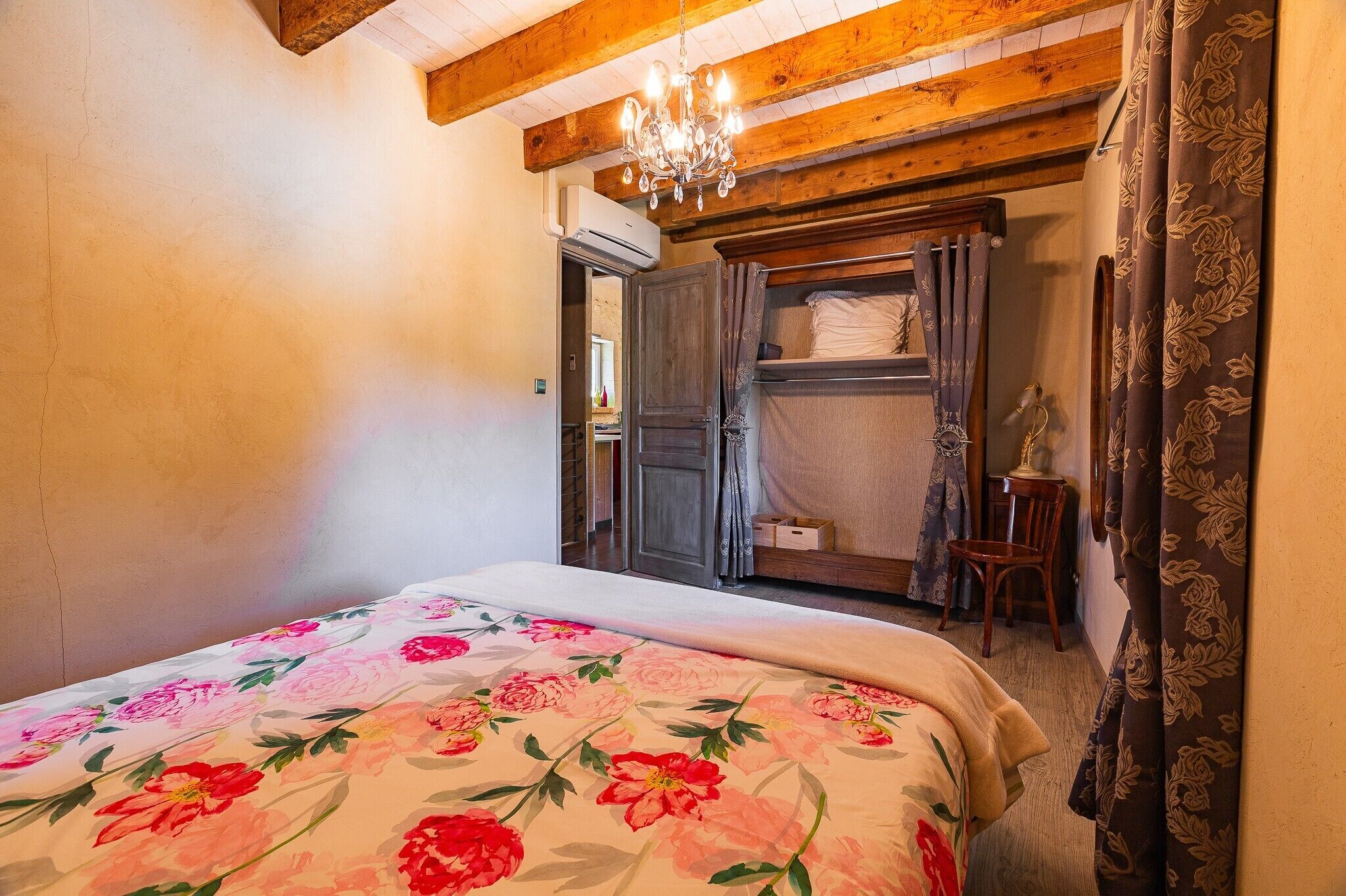 Een slaapkamer met een bed, houten plafond, een kroonluchter, een kledingkast en een stoel.
