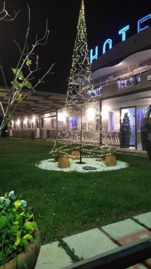 Un hôtel avec un grand sapin de Noël décoré de guirlandes lumineuses dans la cour.
