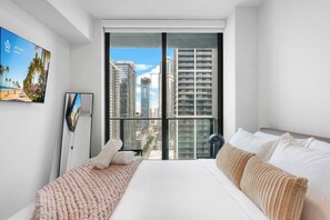 Ein Schlafzimmer mit großem Fenster, einem Bett, einem Nachttisch und einem an der Wand befestigten Fernseher.