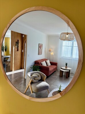 Un salon avec un canapé rouge, un miroir à cadre en bois, une table ronde avec une lampe et une plante en pot.