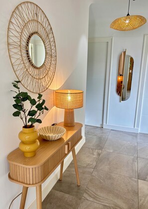 Ein Konsolentisch aus Holz mit einer Lampe, einem Spiegel und einer Vase mit Grünpflanzen.