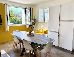 Un coin repas comprenant une table, des chaises, une plante et un réfrigérateur.