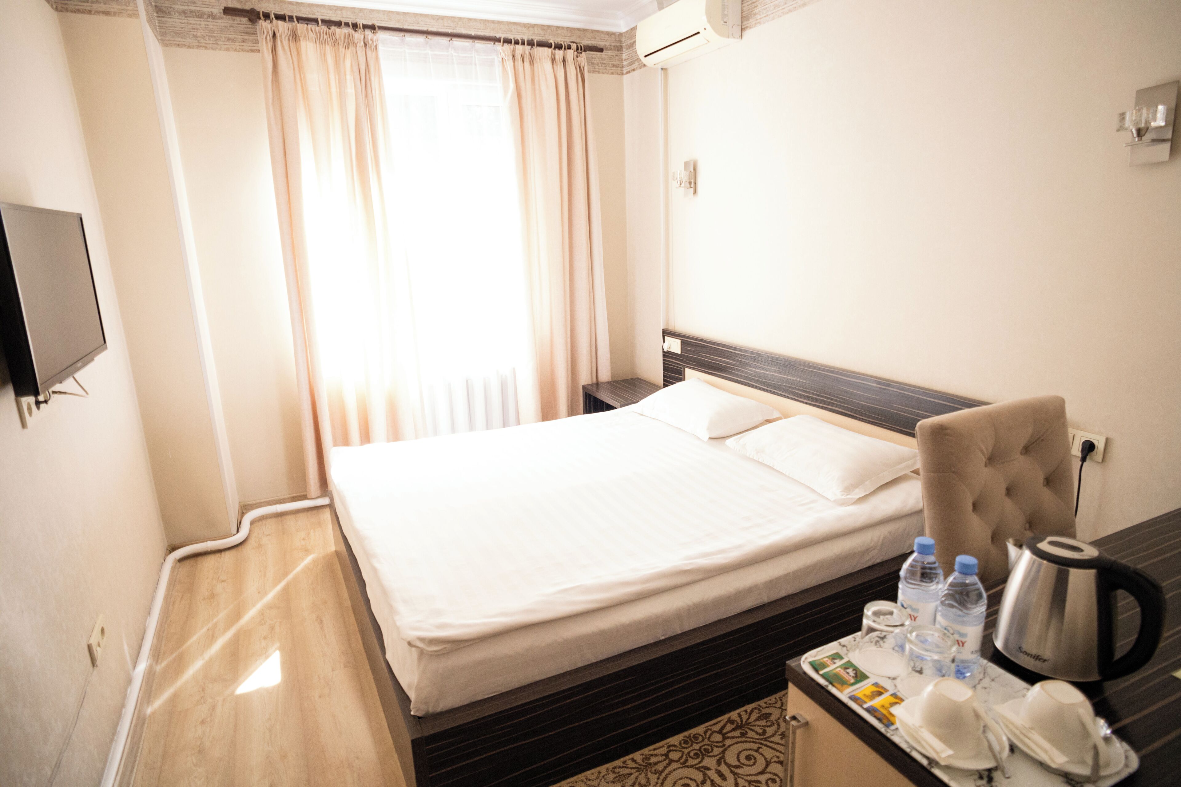A hotel room with a bed, a TV, a coffee maker, and a tray with water bottles and cups.