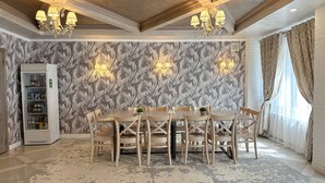A dining area with a marble-patterned wall, chandeliers, a refrigerator, and a patterned rug. - Resident Hotel Almaty (Almaty)