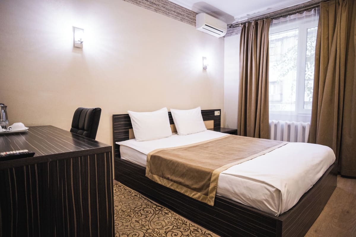 Una habitación de hotel con cama, mesita de noche, silla y ventana con cortinas.