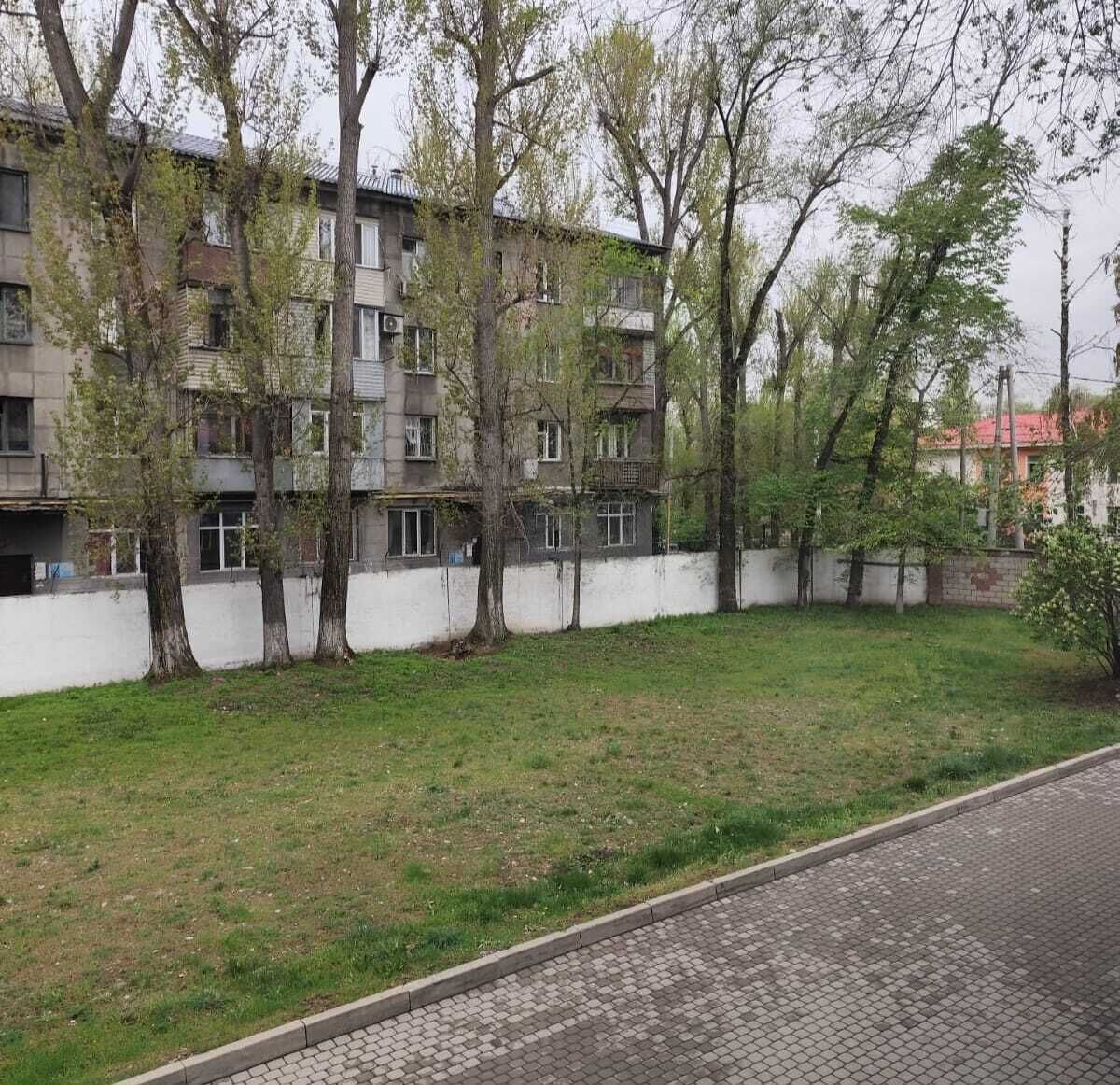A multi-story residential building with a white exterior, surrounded by trees and a grassy area.