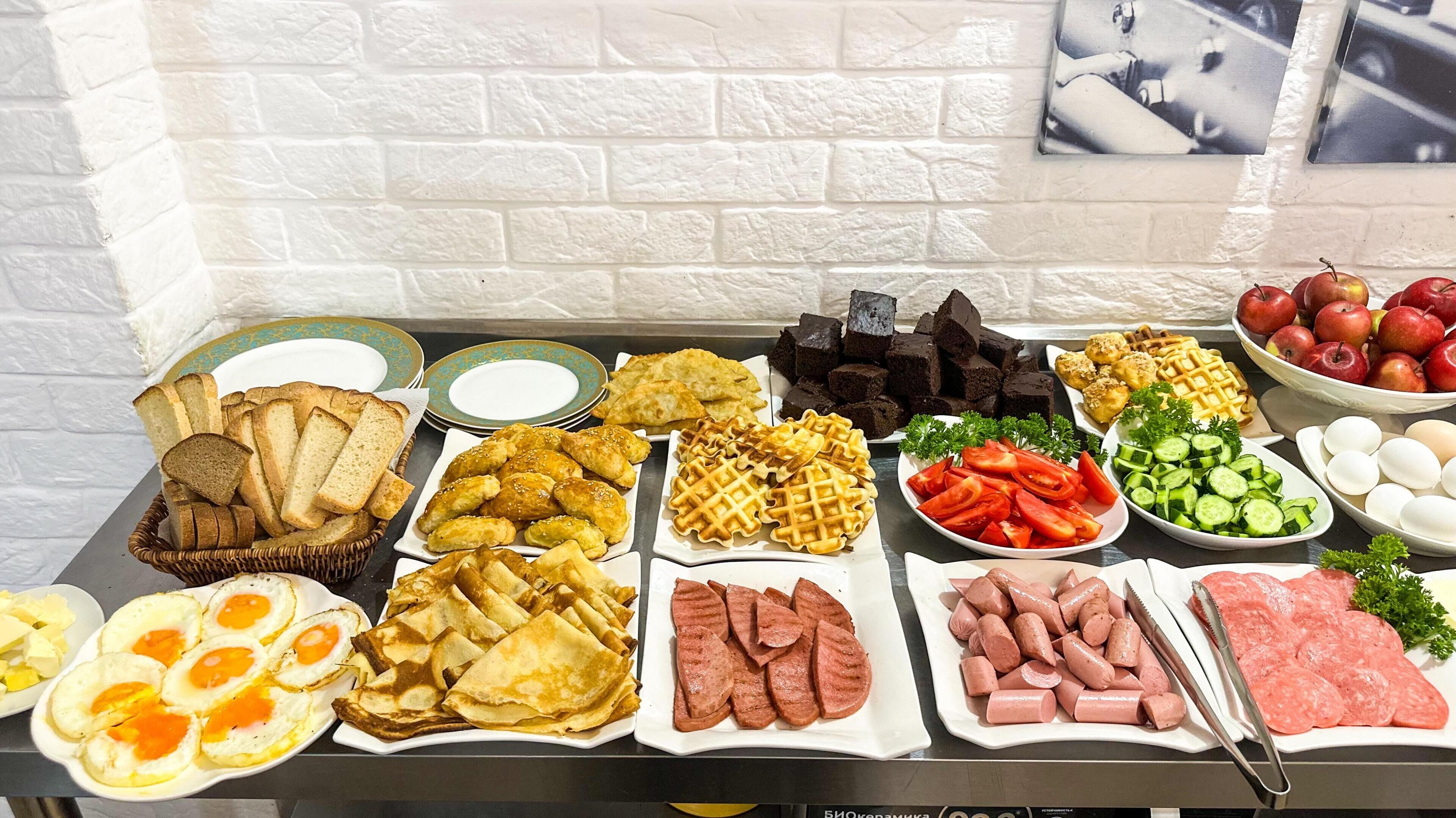 Una mesa de buffet con diversos alimentos, como pan, huevos, salchichas y embutidos en rodajas.
