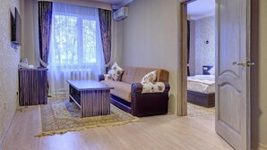 A room with a sofa, a coffee table, a TV, and a bed. - Resident Hotel Almaty (Almaty)