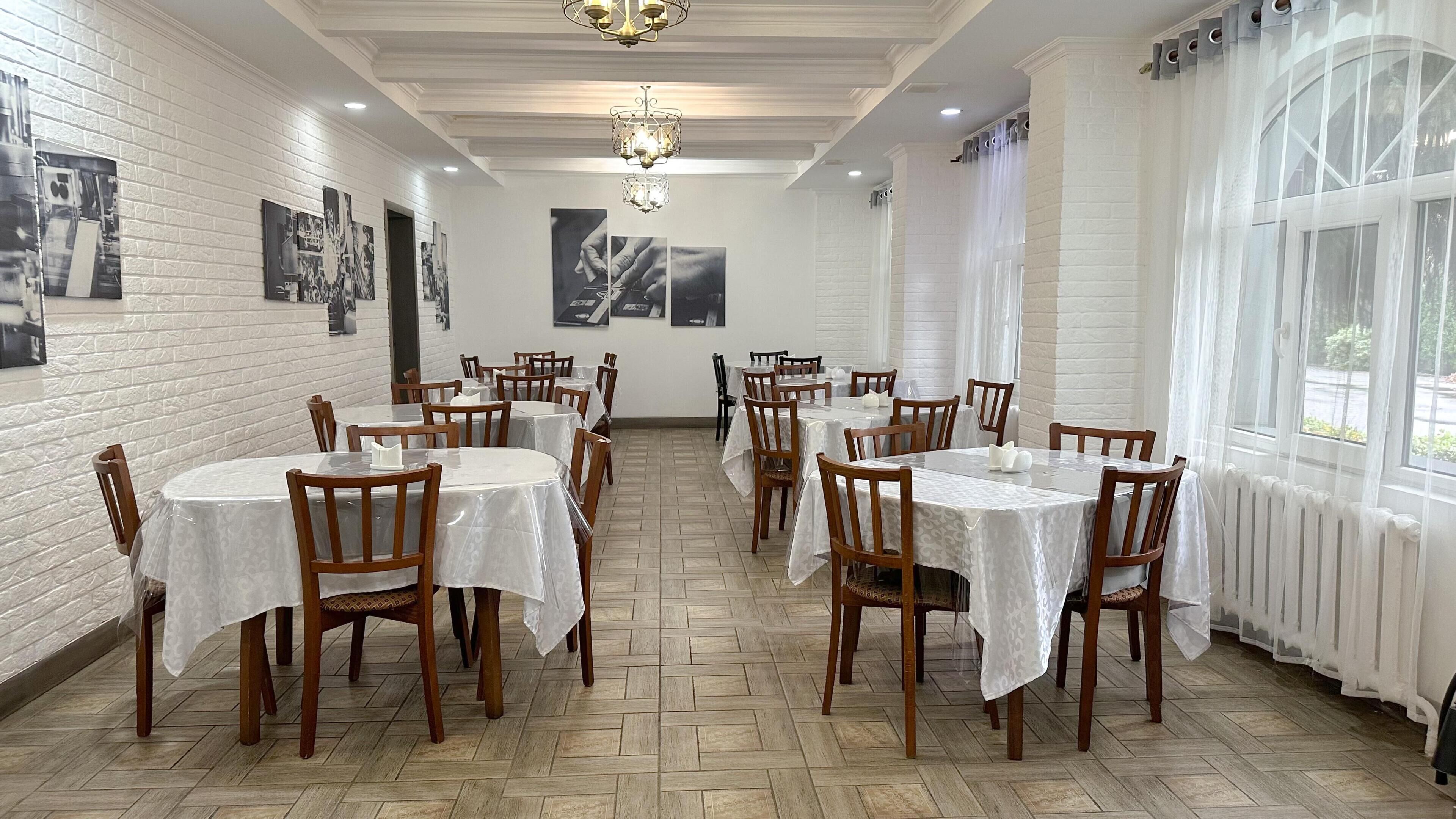 A dining area with round tables, wooden chairs, white walls, and artwork.