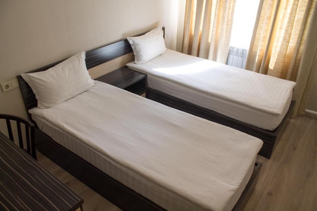 A room with two single beds, a small bedside table, a chair, and a window with curtains.