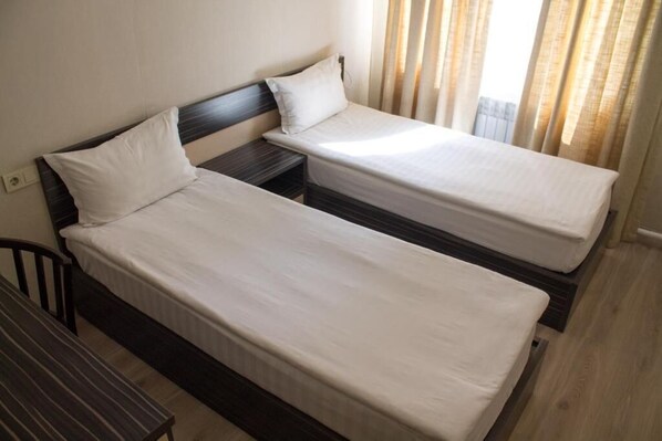 A room with two single beds, a small bedside table, a chair, and a window with curtains. - Resident Hotel Almaty (Almaty)