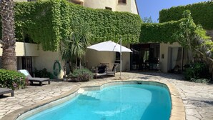 Una piscina con borde de piedra, rodeada de sillas de descanso y una zona de estar cubierta.