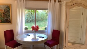 Mesa redonda con dos sillas rojas, un florero con flores y vistas a zonas verdes al exterior.