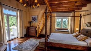 Un dormitorio con cama con dosel, vigas de madera, una araña, un ventanal y vistas al exterior.