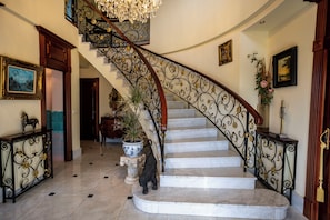 Una gran escalera con barandillas ornamentadas, un candelabro y una planta en maceta.