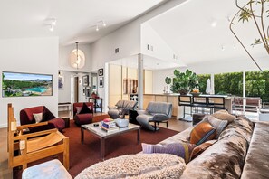 A spacious living area with a large sofa, a coffee table, and a dining area with a view of the outdoors. - El Cid Social - A Bold, Retro‑Chic Palm Springs Escape with Pool, Mountain Views, & BBQ Grill (Palm Springs)