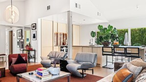 Uma sala de estar moderna com sofá, poltronas, mesa de centro e um espaço de jantar com mesa e cadeiras.