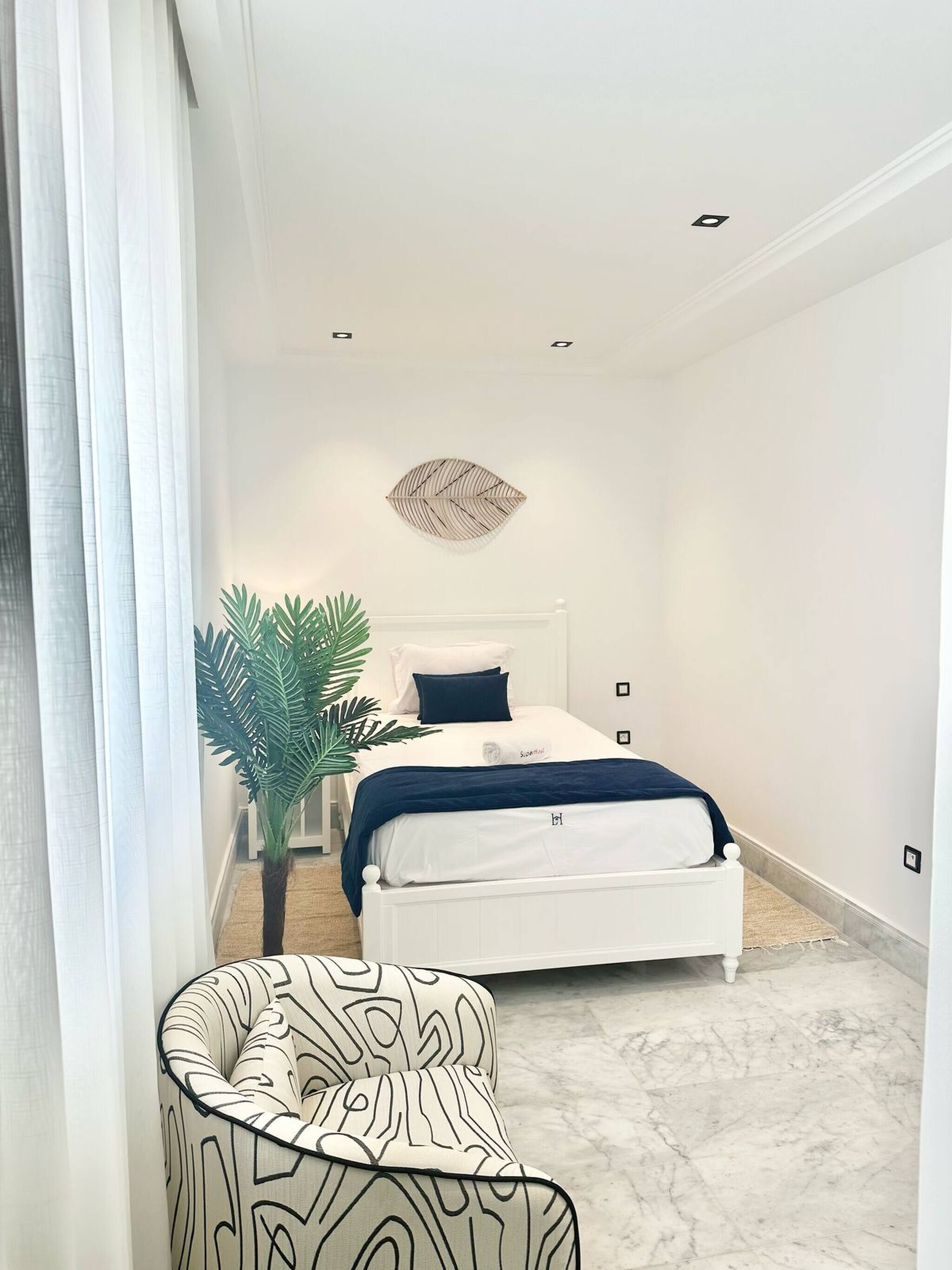 Un dormitorio con cama, planta en maceta, silla y un adorno en la pared.