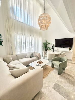 A modern living room with a sectional sofa, a round coffee table, a unique green armchair, a large TV, and a hanging light fixture. - Dahlia Duplex au Coeur de La Marsa (La Marsa)