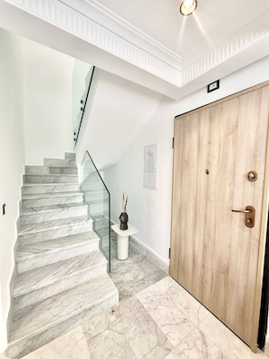 A marble staircase leading to a landing with a glass railing, a wooden door, and a small vase on a pedestal. - Dahlia Duplex au Coeur de La Marsa (La Marsa)