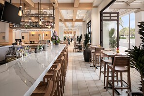 Zona de bar moderna con encimera de mármol, taburetes de madera y una selección de botellas y vasos.