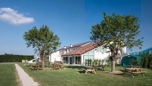 A building with a tiled roof, surrounded by a grassy area with picnic tables and trees. - Nomad Hostel (Treviso)