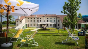 A hotel courtyard with a playground, outdoor seating, and a large umbrella. - Nomad Hostel (Treviso)