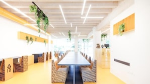 A conference room with a long table, patterned chairs, hanging plants, and a wooden ceiling. - Nomad Hostel (Treviso)