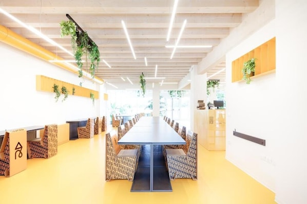 Un salón de conferencias con una larga mesa, sillas estampadas, plantas colgantes y techo de madera.