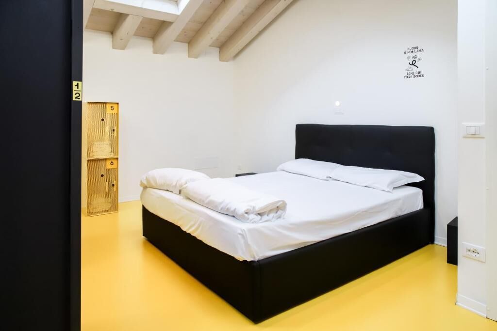 Una cama individual con cabecera negra en una habitación con suelo amarillo y paredes blancas.