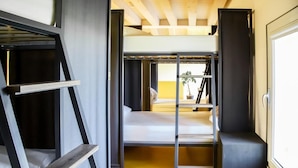A compact room with a bunk bed, a small wooden shelf, and a window with a view. - Nomad Hostel (Treviso)