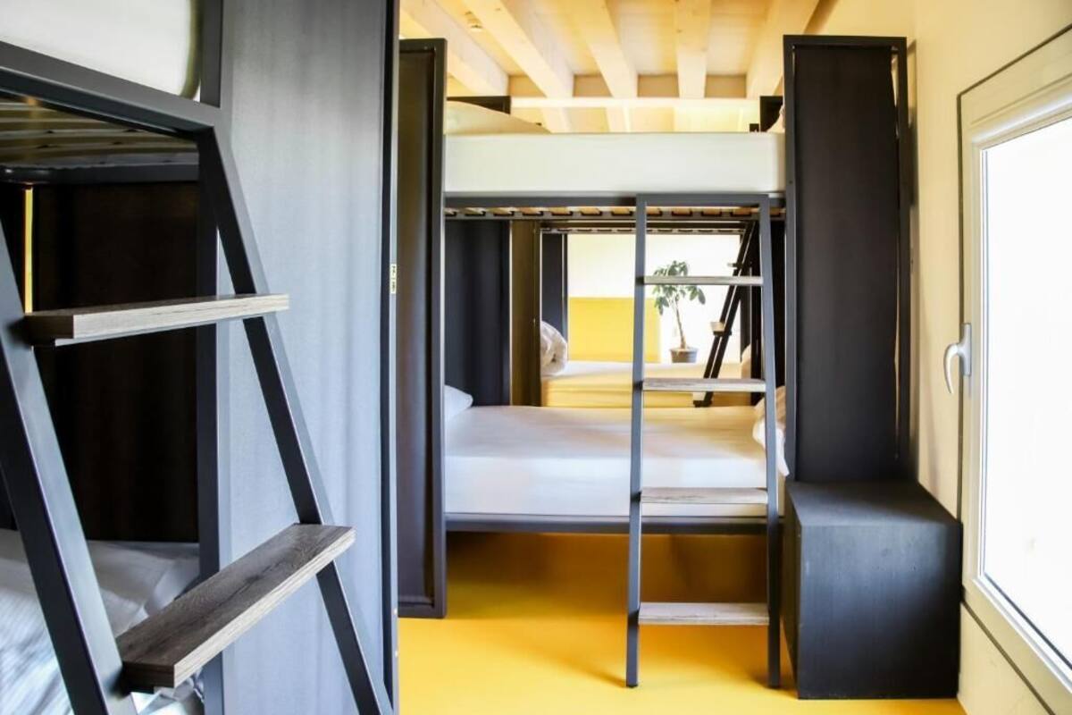Une petite pièce avec un lit superposé, une petite étagère en bois et une fenêtre donnant sur un paysage agréable.