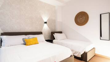 A hotel room with two beds, a textured wall, a wall-mounted light, a woven wall decoration, and a framed picture.