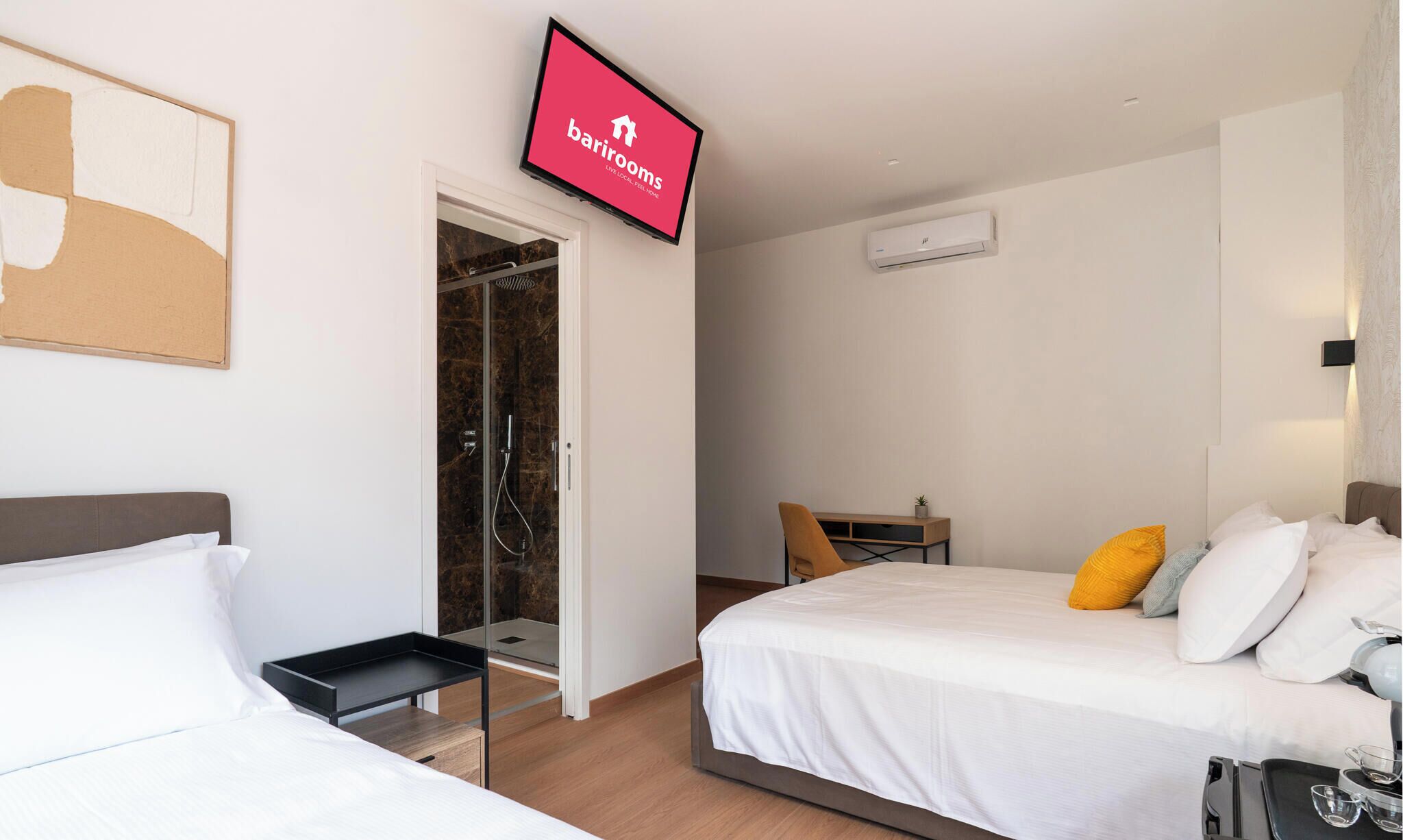 A hotel room with a bed, a desk, a chair, a TV, and a shower area.