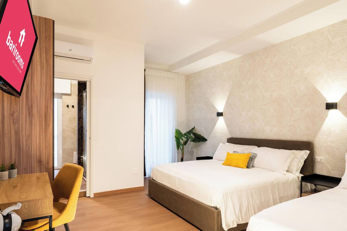 Habitación de hotel con cama, mesitas de noche, un escritorio con silla, televisor y una planta.