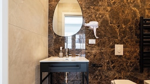 Un baño con pared de mármol, lavamanos con espejo, secador de pelo y retrete.